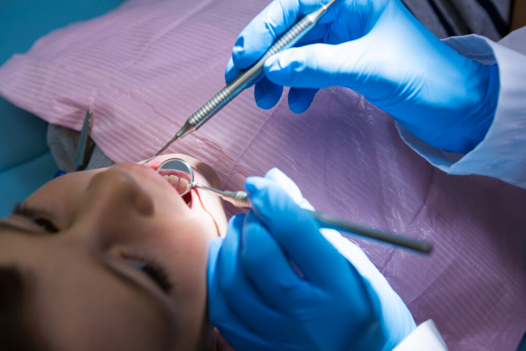 CDBS dentist checking a young patient's teeth with a dental mirror and probe