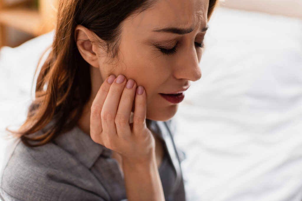 Woman holding her cheek with her eyes closed in pain, which could be a sign of a chipped tooth